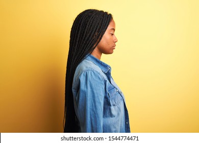 Joven afroamericana con camiseta de denim sobre fondo amarillo aislado mirando al lado, perfil relajado posar con cara natural y sonrisa segura.