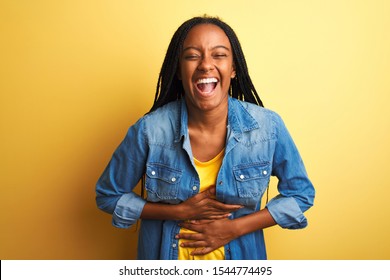 Young african american woman wearing denim shirt standing over isolated yellow background smiling and laughing hard out loud because funny crazy joke with hands on body.