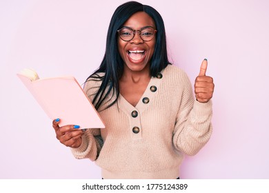 Young African American Woman Wearing Glasses Holding Book Screaming Proud, Celebrating Victory And Success Very Excited With Raised Arms 