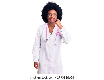 Young African American Woman Wearing Doctor Coat And Stethoscope Pointing With Hand Finger To Face And Nose, Smiling Cheerful. Beauty Concept 