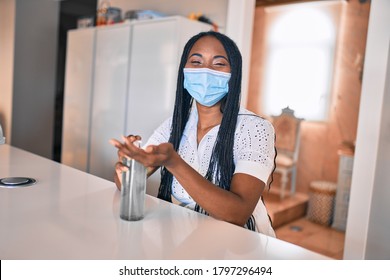 Young African American Woman Wearing Medical Mask Using Sanitizer Hand Gel At Home