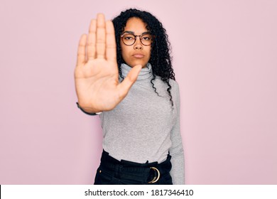 Young african american woman wearing turtleneck sweater and glasses over pink background doing stop sing with palm of the hand. Warning expression with negative and serious gesture on the face.
