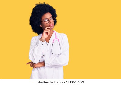 Young African American Woman Wearing Doctor Coat And Stethoscope With Hand On Chin Thinking About Question, Pensive Expression. Smiling With Thoughtful Face. Doubt Concept. 