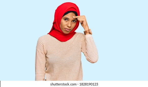 Young African American Woman Wearing Traditional Islamic Hijab Scarf Pointing Unhappy To Pimple On Forehead, Ugly Infection Of Blackhead. Acne And Skin Problem 