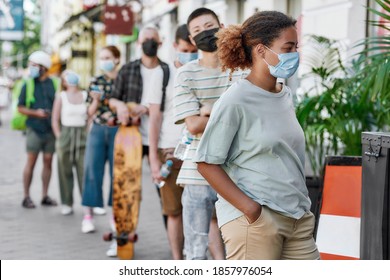 Young African American Woman Wearing Mask Waiting, Standing In Line With Other People, Respecting Social Distancing To Collect Takeaway Order From The Pickup Point During Coronavirus Lockdown