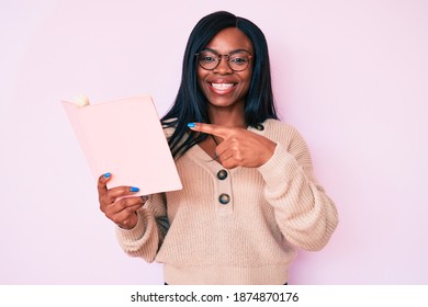 Young African American Woman Wearing Glasses Holding Book Smiling Happy Pointing With Hand And Finger 