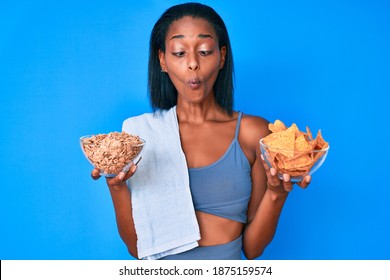 Young African American Woman Wearing Sportswear Holding Nachos And Cereal Making Fish Face With Mouth And Squinting Eyes, Crazy And Comical. 