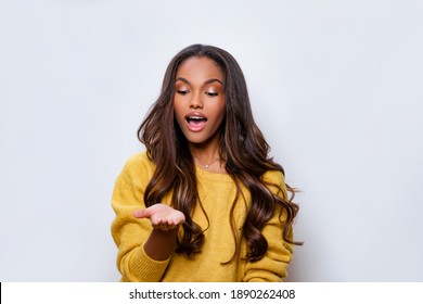 Young african american woman wearing casual clothes smiling with hand palm receiving or giving gesture hold and protection. Black Girl model looks at hand with admiration, mouth   open.           