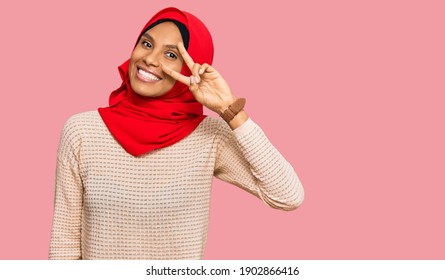 Young African American Woman Wearing Traditional Islamic Hijab Scarf Doing Peace Symbol With Fingers Over Face, Smiling Cheerful Showing Victory 