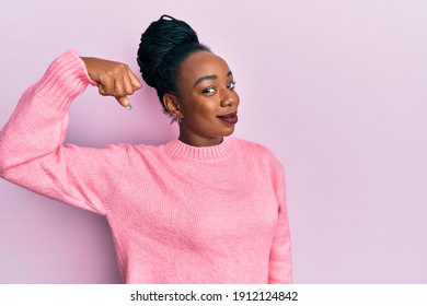 Young african american woman wearing casual winter sweater strong person showing arm muscle, confident and proud of power 