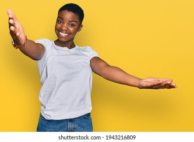 Young African American Woman Wearing Casual White T Shirt Looking At The Camera Smiling With Open Arms For Hug. Cheerful Expression Embracing Happiness. 