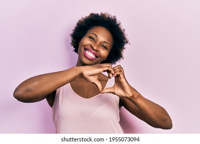 Young african american woman wearing casual sleeveless t shirt smiling in love doing heart symbol shape with hands. romantic concept. 