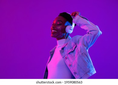 Young African American woman wearing headphones listening to music and dancing in futuristic purple cyberpunk neon light background - Powered by Shutterstock