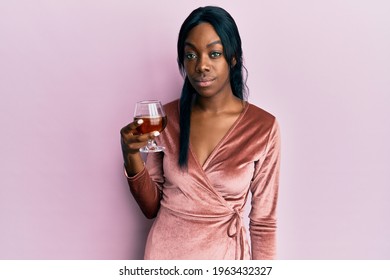 Young African American Woman Wearing Sexy Party Dress Holding Cocktail Thinking Attitude And Sober Expression Looking Self Confident 