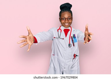 Young African American Woman Wearing Doctor Uniform And Stethoscope Looking At The Camera Smiling With Open Arms For Hug. Cheerful Expression Embracing Happiness. 