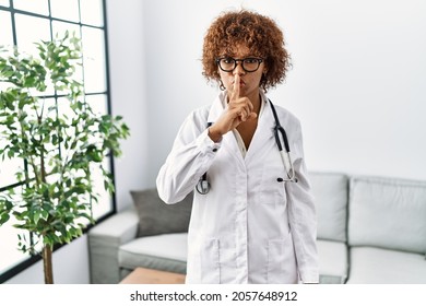 Young african american woman wearing doctor uniform and stethoscope asking to be quiet with finger on lips. silence and secret concept. 