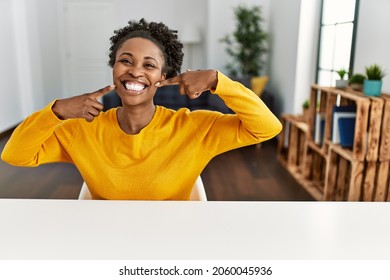 Young african american woman wearing casual clothes sitting on the table at home smiling cheerful showing and pointing with fingers teeth and mouth. dental health concept. 