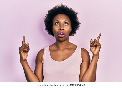 Young African American Woman Wearing Casual Sleeveless T Shirt Amazed And Surprised Looking Up And Pointing With Fingers And Raised Arms. 