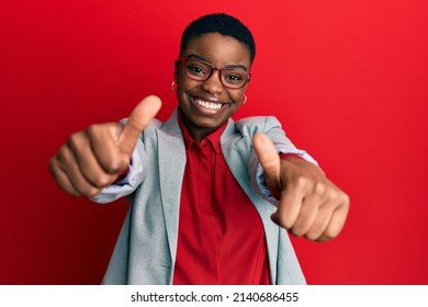 Young african american woman wearing business jacket and glasses approving doing positive gesture with hand, thumbs up smiling and happy for success. winner gesture. 