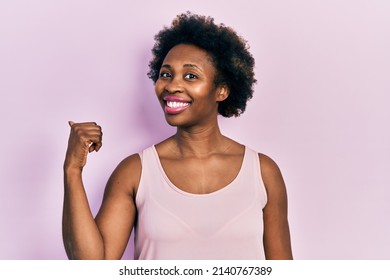 Young African American Woman Wearing Casual Sleeveless T Shirt Smiling With Happy Face Looking And Pointing To The Side With Thumb Up. 