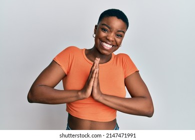 Young african american woman wearing casual orange t shirt praying with hands together asking for forgiveness smiling confident. 