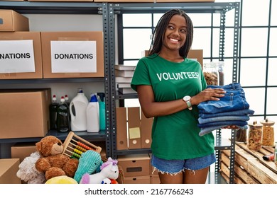 Young african american woman wearing volunteer uniform holding folded jeans at charity center
