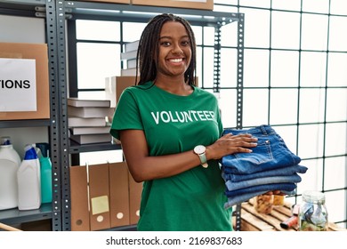 Young african american woman wearing volunteer uniform holding folded jeans at charity center