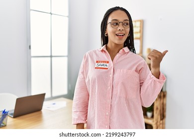 Young African American Woman Wearing Hello My Name Is Sticker Identification Pointing Thumb Up To The Side Smiling Happy With Open Mouth 