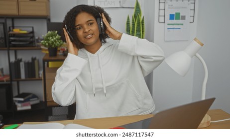 Young african american woman wearing headphones in an office, working indoors with books, desk, and plants, highlighting a modern workspace setting. - Powered by Shutterstock