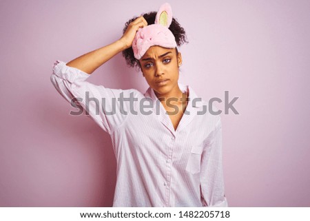Young african american woman wearing pajama and mask over isolated pink background confuse and wondering about question. Uncertain with doubt, thinking with hand on head. Pensive concept.