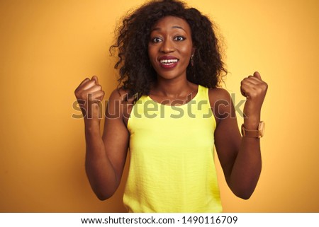 Young african american woman wearing t-shirt standing over isolated yellow background celebrating surprised and amazed for success with arms raised and open eyes. Winner concept.