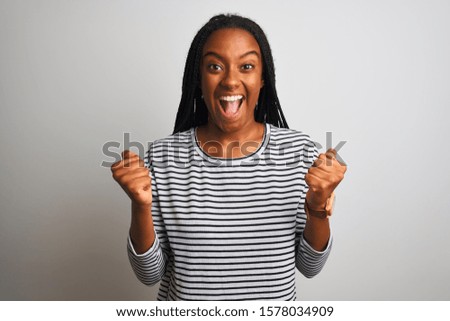Young african american woman wearing striped t-shirt standing over isolated white background celebrating surprised and amazed for success with arms raised and open eyes. Winner concept.