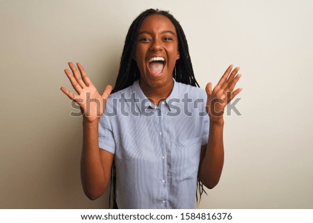 Young african american woman wearing striped shirt standing over isolated white background celebrating crazy and amazed for success with arms raised and open eyes screaming excited. Winner concept