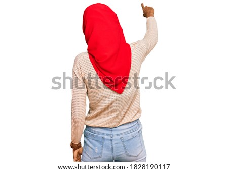 Young african american woman wearing traditional islamic hijab scarf posing backwards pointing ahead with finger hand 
