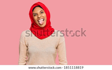 Young african american woman wearing traditional islamic hijab scarf sticking tongue out happy with funny expression. emotion concept. 