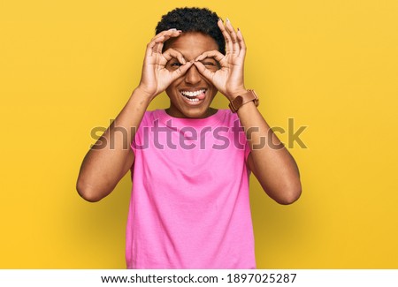 Young african american woman wearing casual clothes doing ok gesture like binoculars sticking tongue out, eyes looking through fingers. crazy expression. 