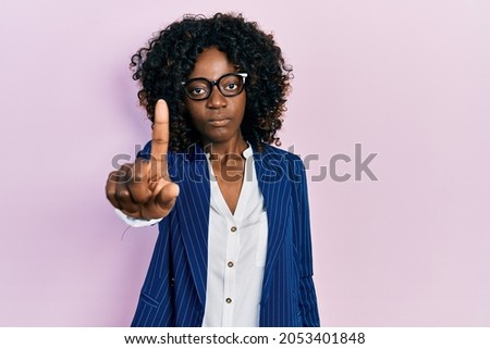 Young african american woman wearing business clothes and glasses pointing with finger up and angry expression, showing no gesture 