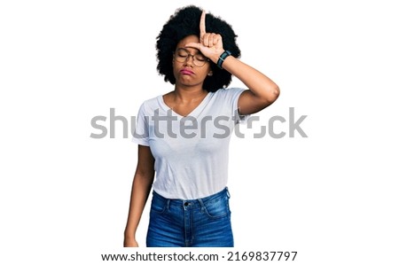 Young african american woman wearing casual white t shirt making fun of people with fingers on forehead doing loser gesture mocking and insulting. 