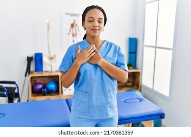 Young African American Woman Working At Pain Recovery Clinic Smiling With Hands On Chest With Closed Eyes And Grateful Gesture On Face. Health Concept. 