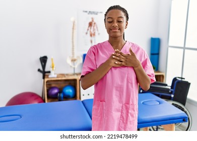 Young African American Woman Working At Pain Recovery Clinic Smiling With Hands On Chest With Closed Eyes And Grateful Gesture On Face. Health Concept. 