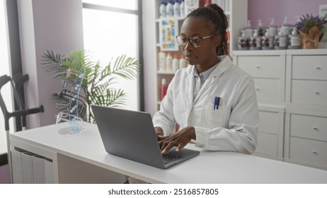 Young, african, american, woman working in a pharmacy typing on laptop while wearing glasses in a clean, organized drugstore with shelves of products in the background - Powered by Shutterstock