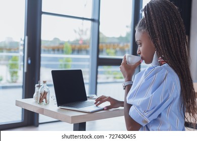 Young African American Woman Working With Laptop And Drinking Coffee At Cafe