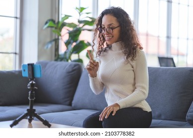 Young African American women wearing eyeglasses live streaming training on the sofa through the application from smartphone to social media during the coronavirus outbreak. - Shutterstock ID 2103778382