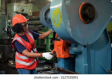 Young African American Women Worker In Safety Uniform, Hard Hat, Vest And Glove In Industrial Manufacturer Factory Are Working On Heavy Machinery.