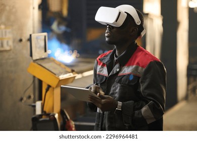 Young African American worker of factory in vr headset using tablet while operating industrial machine during technical production process - Powered by Shutterstock