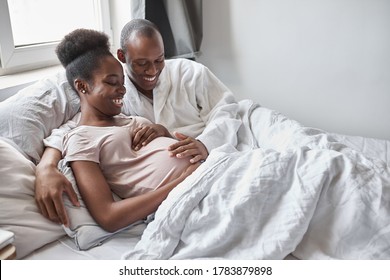 young african black family will have replenishment soon, pregnant woman and man lie on bed in the morning, at home