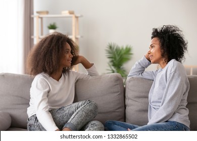 Young african black mother chatting with teen daughter, older sister or friendly nanny and adolescent girl talking sitting together on sofa at home. Good relations different aged people trust concept - Shutterstock ID 1332865502