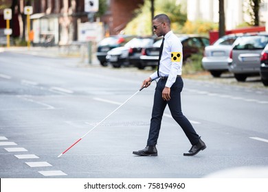 Young African Blind Man Wearing Armband Walking With Stick Crossing Road