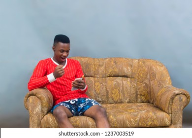A young African boy sitting on a couch with his phone excited