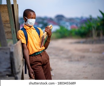 young African boy in uniform, with back pack and books in the hand-Black guy with face mask-out door school concept